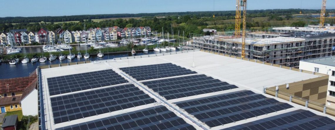 Luftbild vom Parkahsu am Ryck. Im Vordergrund die PV-Dachanlage, im Hintergrund die Marina Holzteich mit Segelschiffen im Hafen. Copyrihgt Inselwerke eG