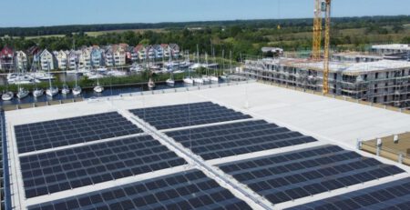 Luftbild vom Parkahsu am Ryck. Im Vordergrund die PV-Dachanlage, im Hintergrund die Marina Holzteich mit Segelschiffen im Hafen. Copyrihgt Inselwerke eG
