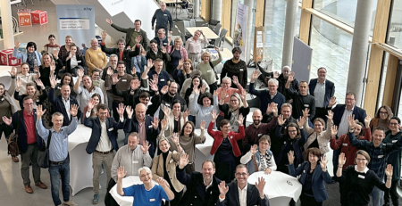 Eine Menschengruppe steht i einem lichtdurchfluteten Foyer und winkt in die Kamera