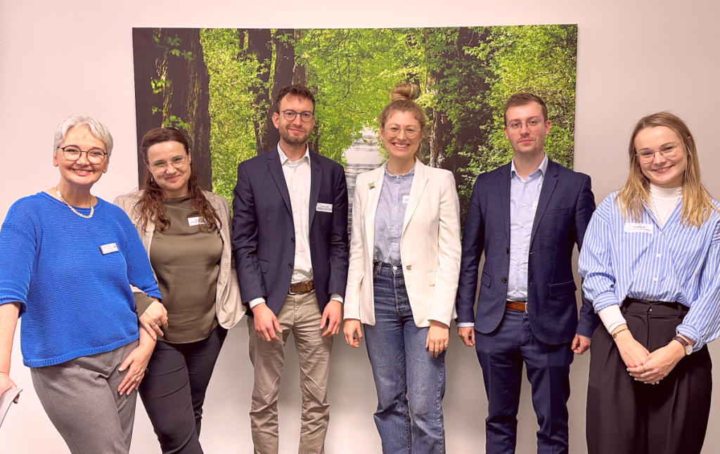 Das Orgateam der Veranstaltung mit Gudrun Stark, Stefanie Beitz, Jonathan Metz, Carla Fee Weisse, Jens Bieker und Nikola Hefner. Sie alle stehen in einem Raum im Hintergrund ist ein großes Foto mit einem Wald zu sehen.