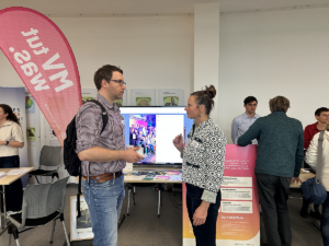 Dr. Annette Teltewskoi um Gespräch mit Sören Meier aus dem Wirtschaftministerium. Im Hintergrund ist ein Bildschirm zu sehen, auf dem ein Video gezeigt wird.