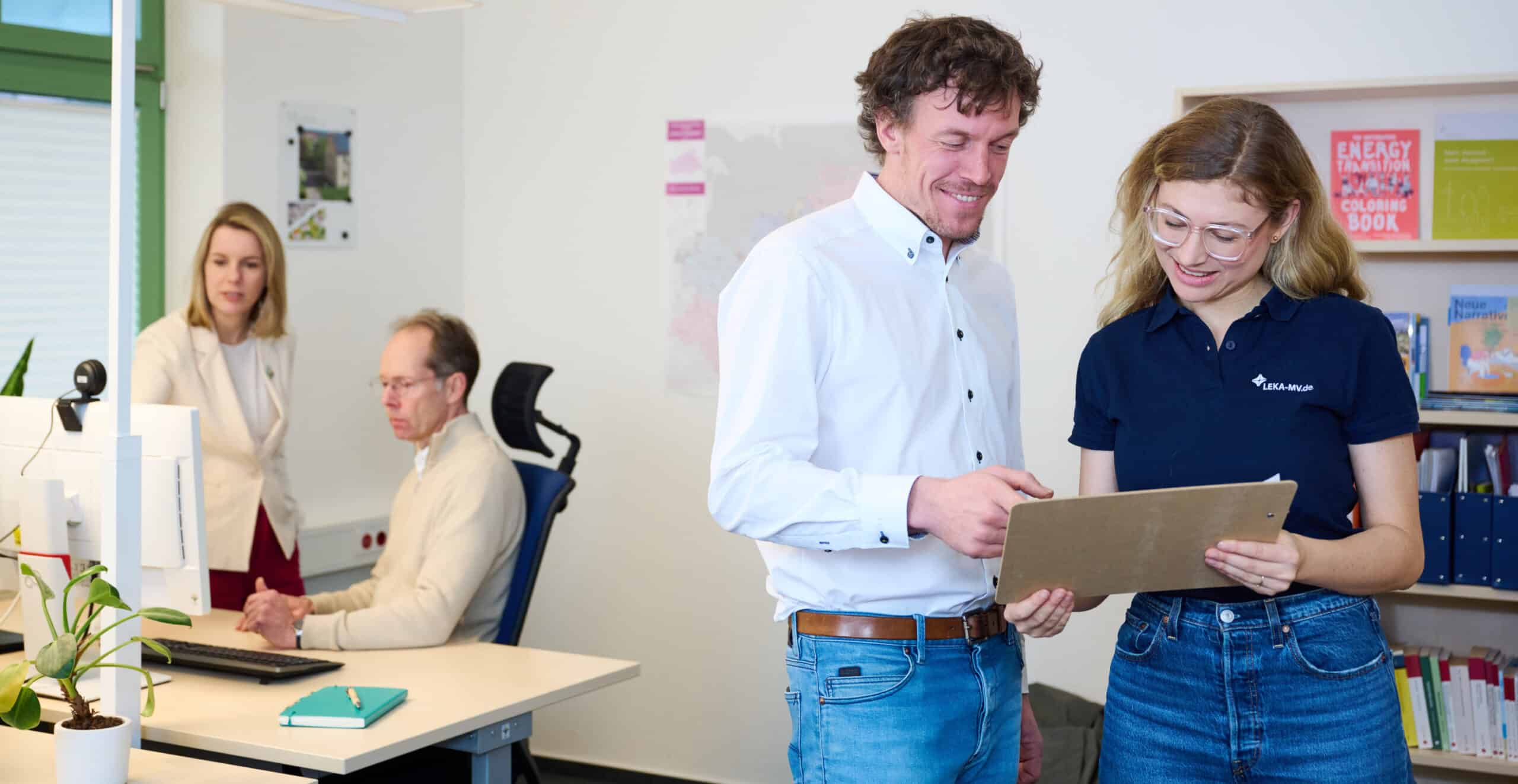 Vier Leka-Mitarbeiter im Büro, im Vordergrund halten ein Mann und eine Frau ein Dokument in der Hand und sprechen darüber