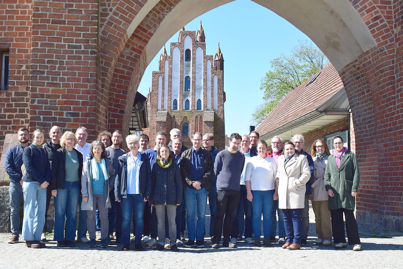 Eine Menschengruppe von 26 Teilnehmern steht vor dem Friedländer Tor. Alle wenden sich dem Fotografen zu.