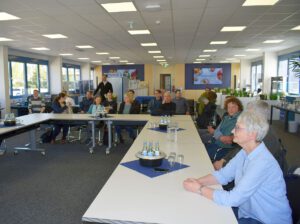 Eine Menschengruppe sitzt an einem U-förmigen Tisch. Auf dem Tisch stehen Getränke.